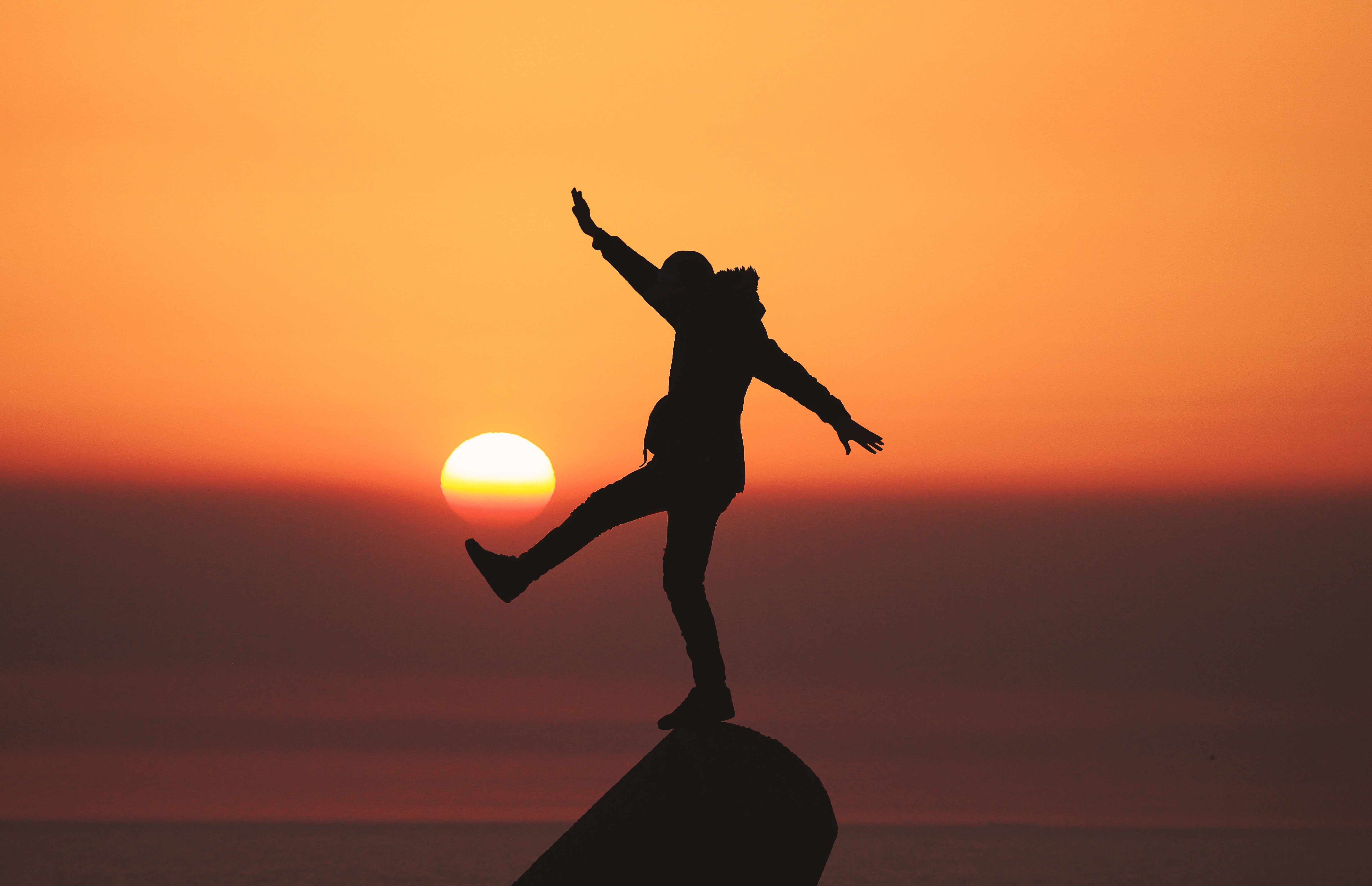 A man is balancing on a rock in front of a sunset