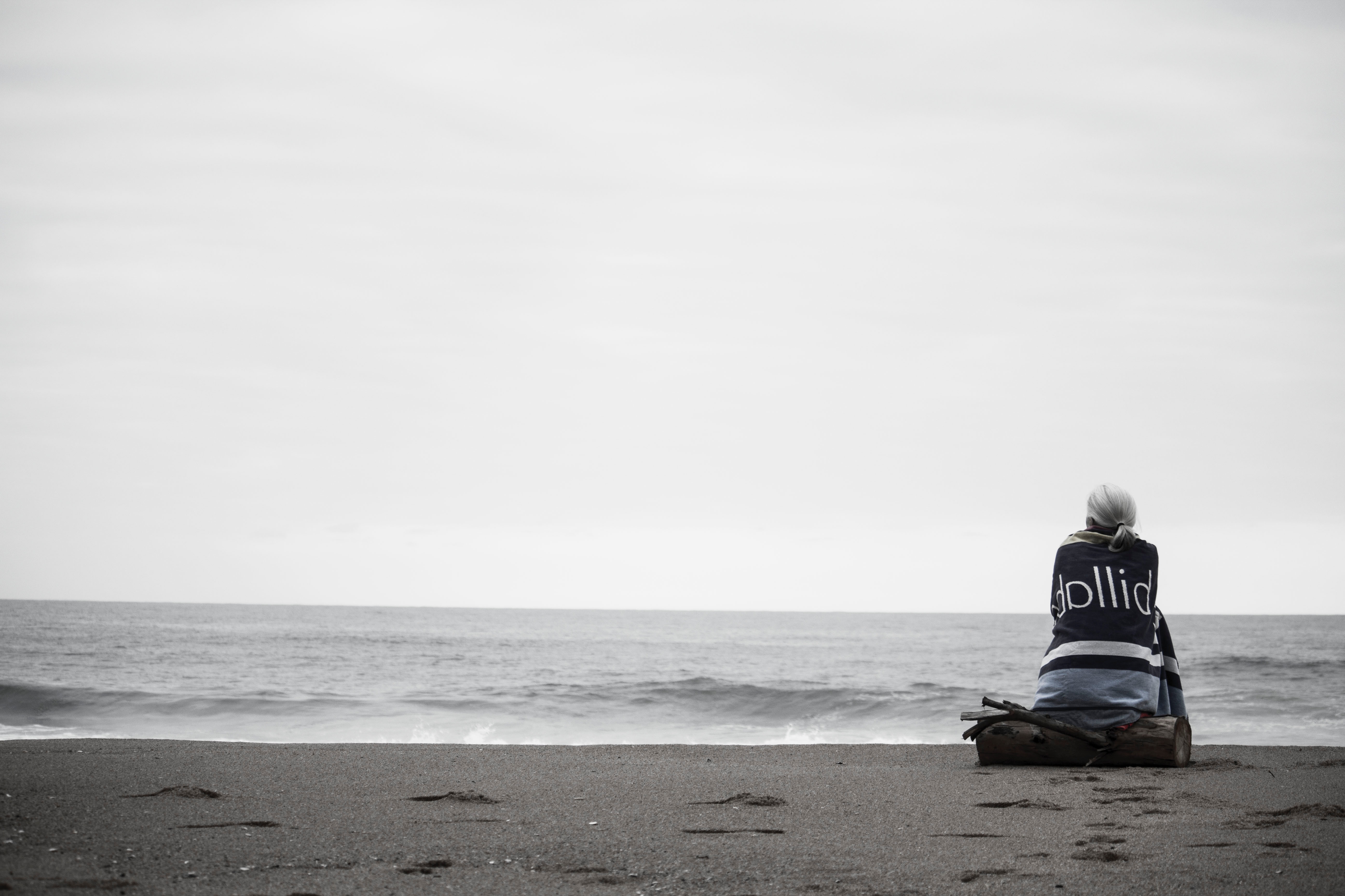 Woman sitting alone on the beach wrapped in a blanket