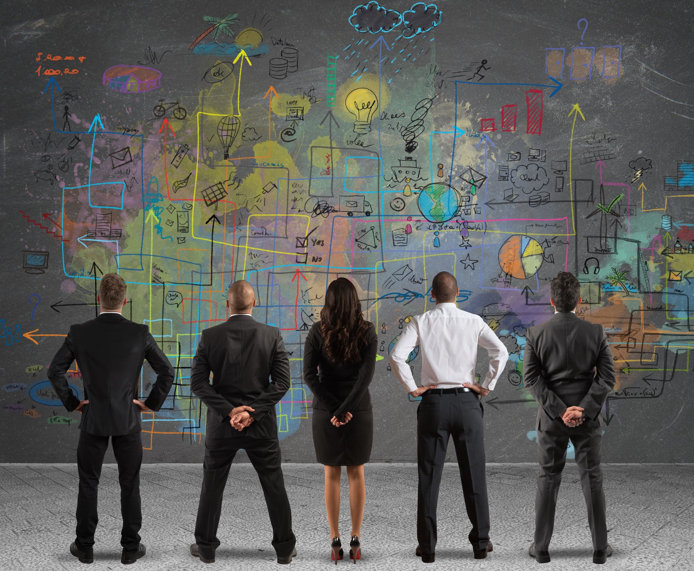 A business team looks at a large strategy painted on the wall.