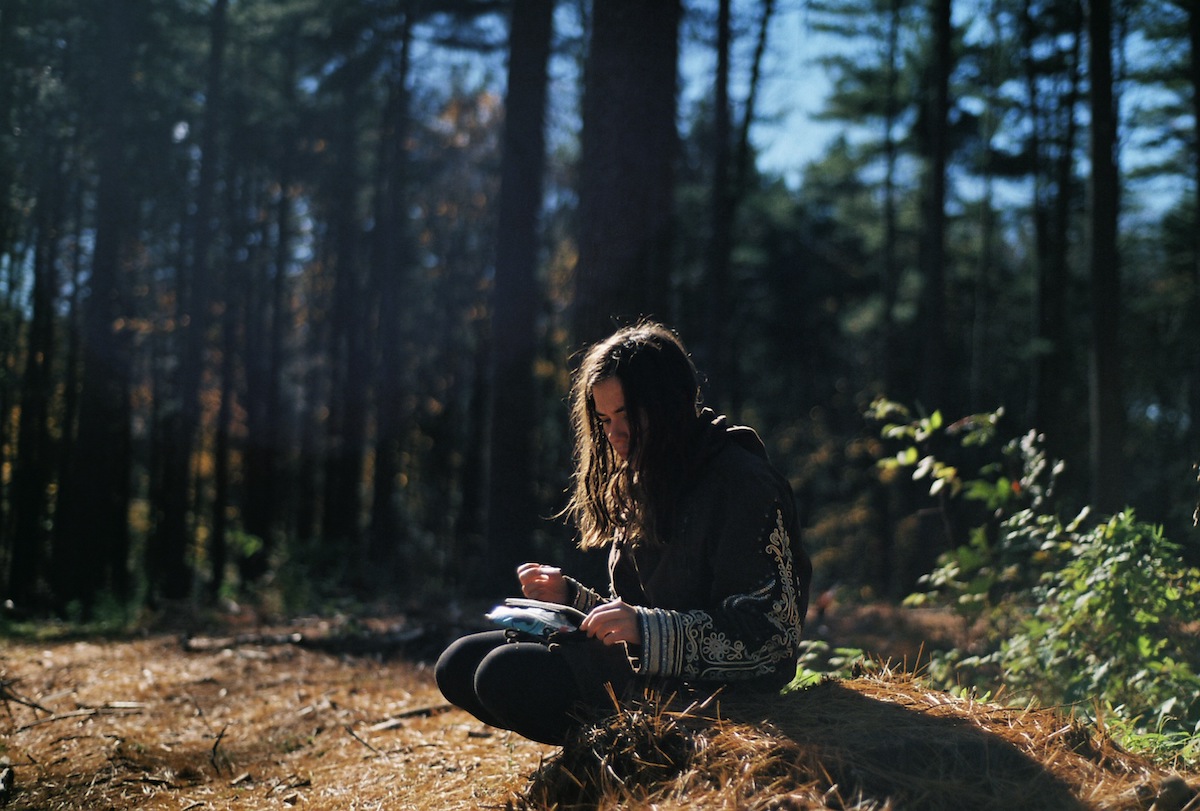 A girl crouches down in the forest to journal