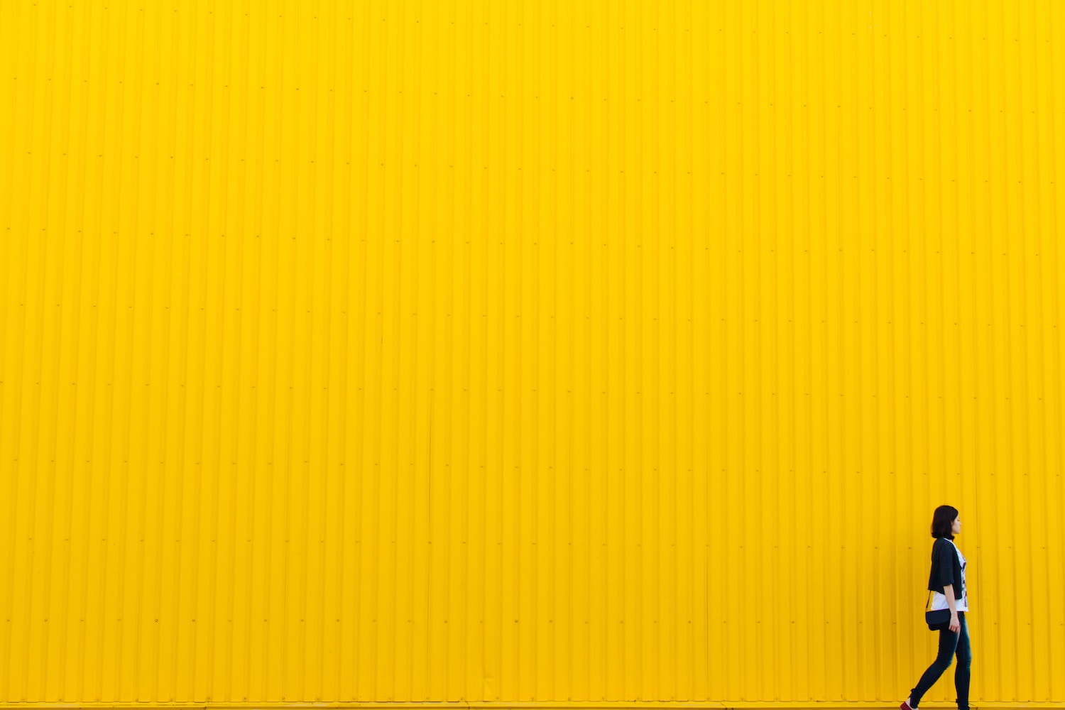 Woman in black walks past large yellow wall