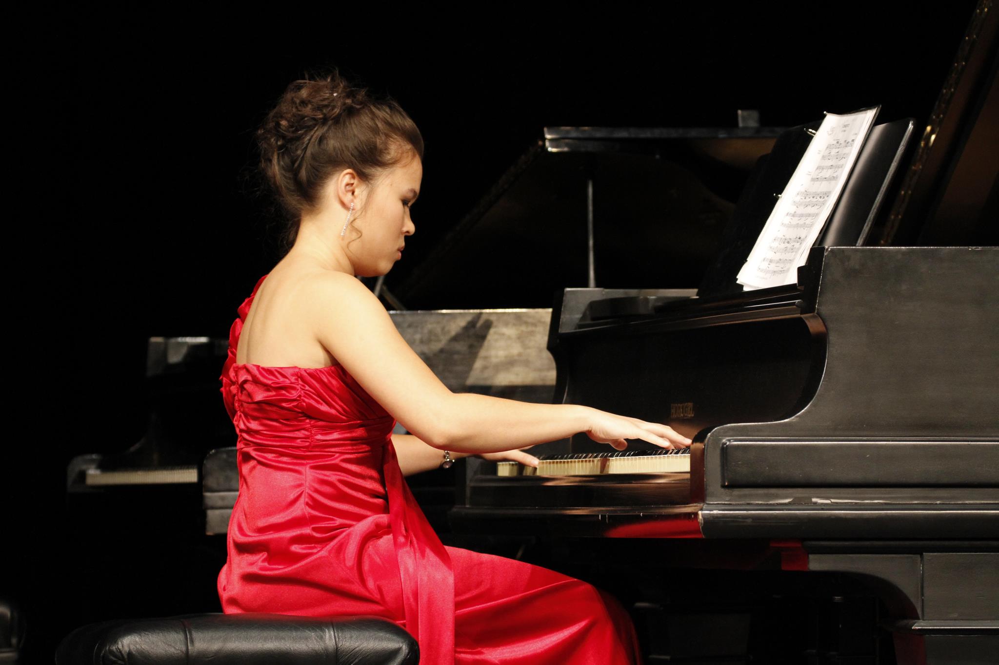 Abby Edwards sitting at a piano in a red dress performing at her senior recital.