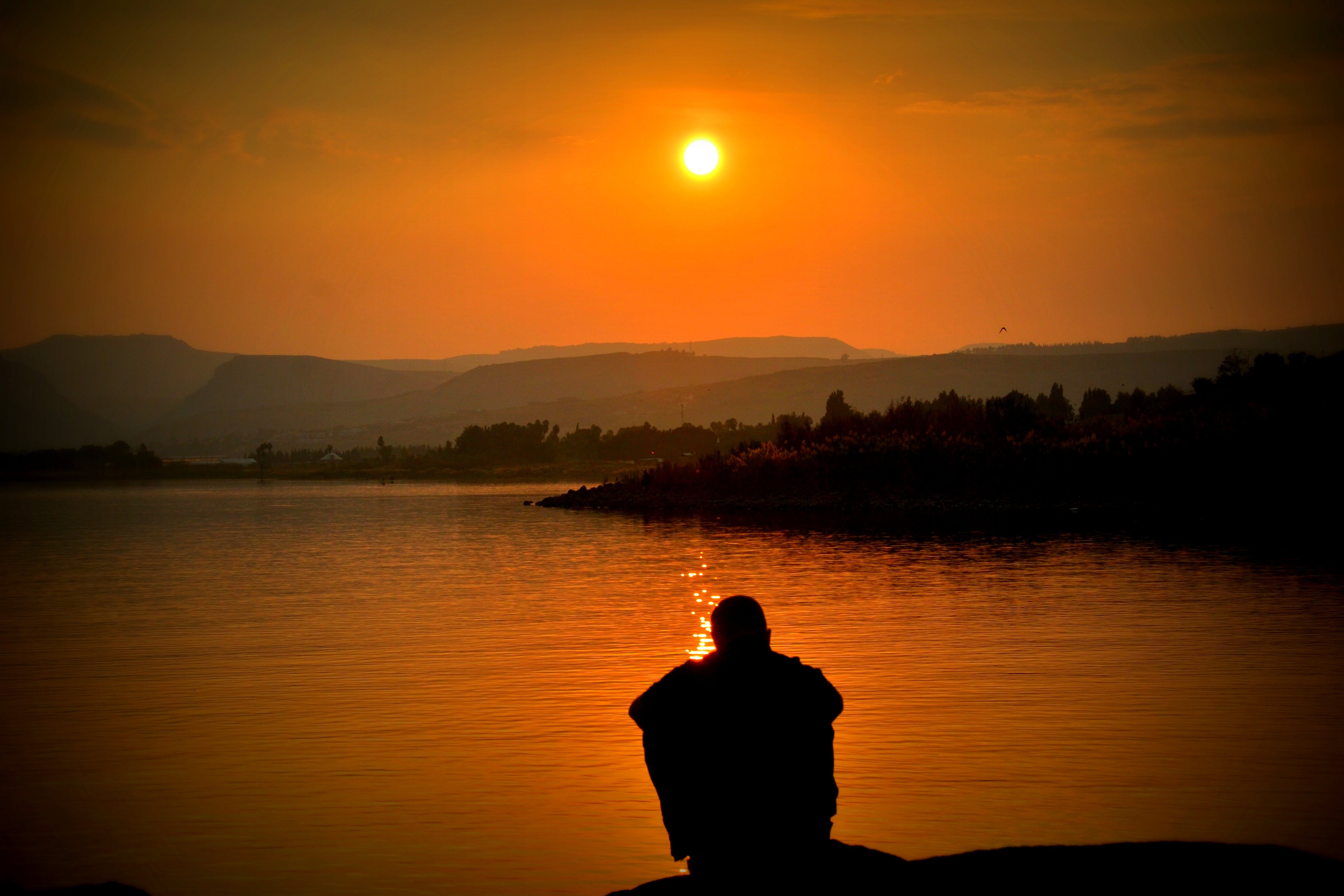 Silhouette of a Man Sitting on the Edge of a Lake Watching the Sunset