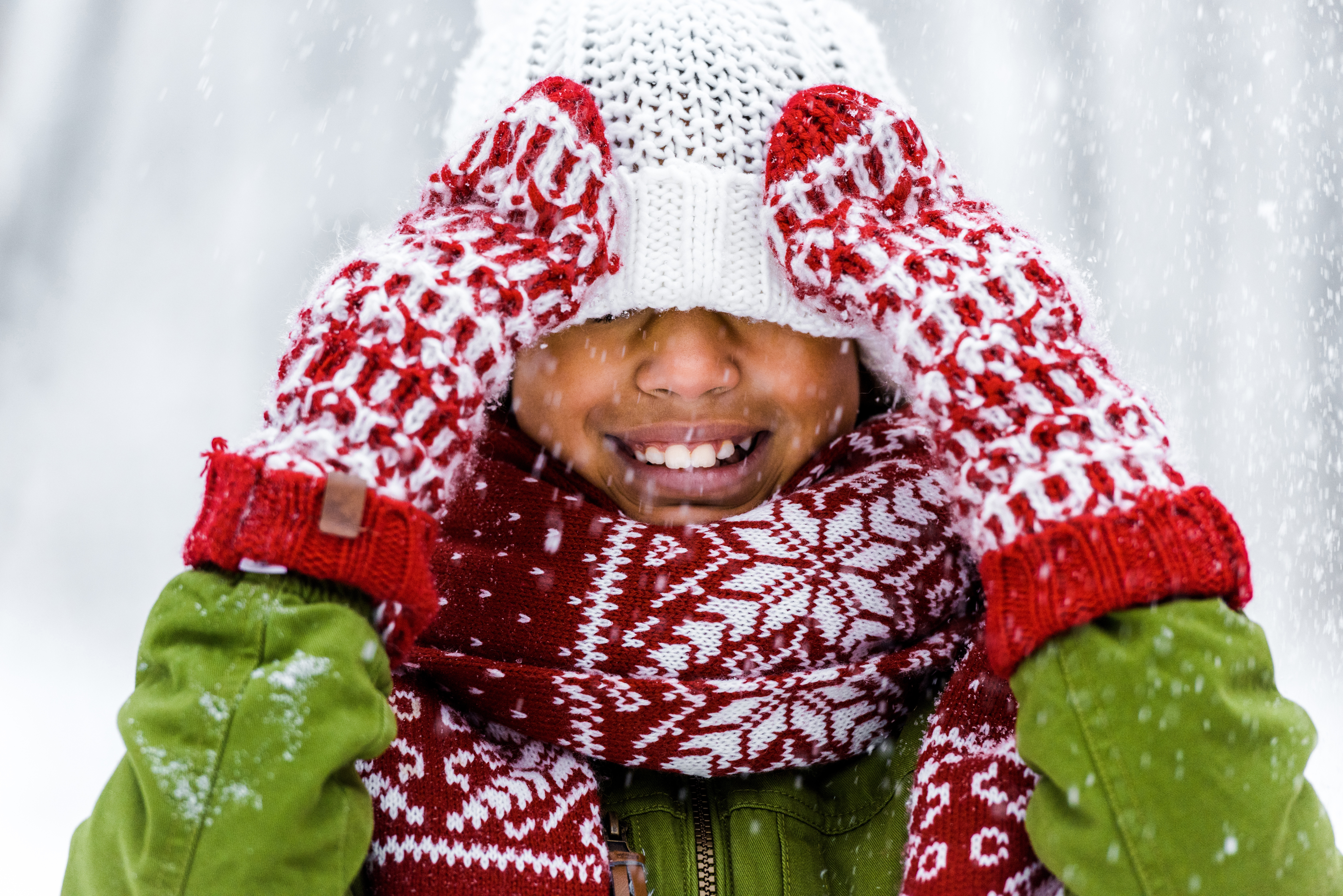 Cute African American child with knitted hat pulled over eyes smiling during snowfall