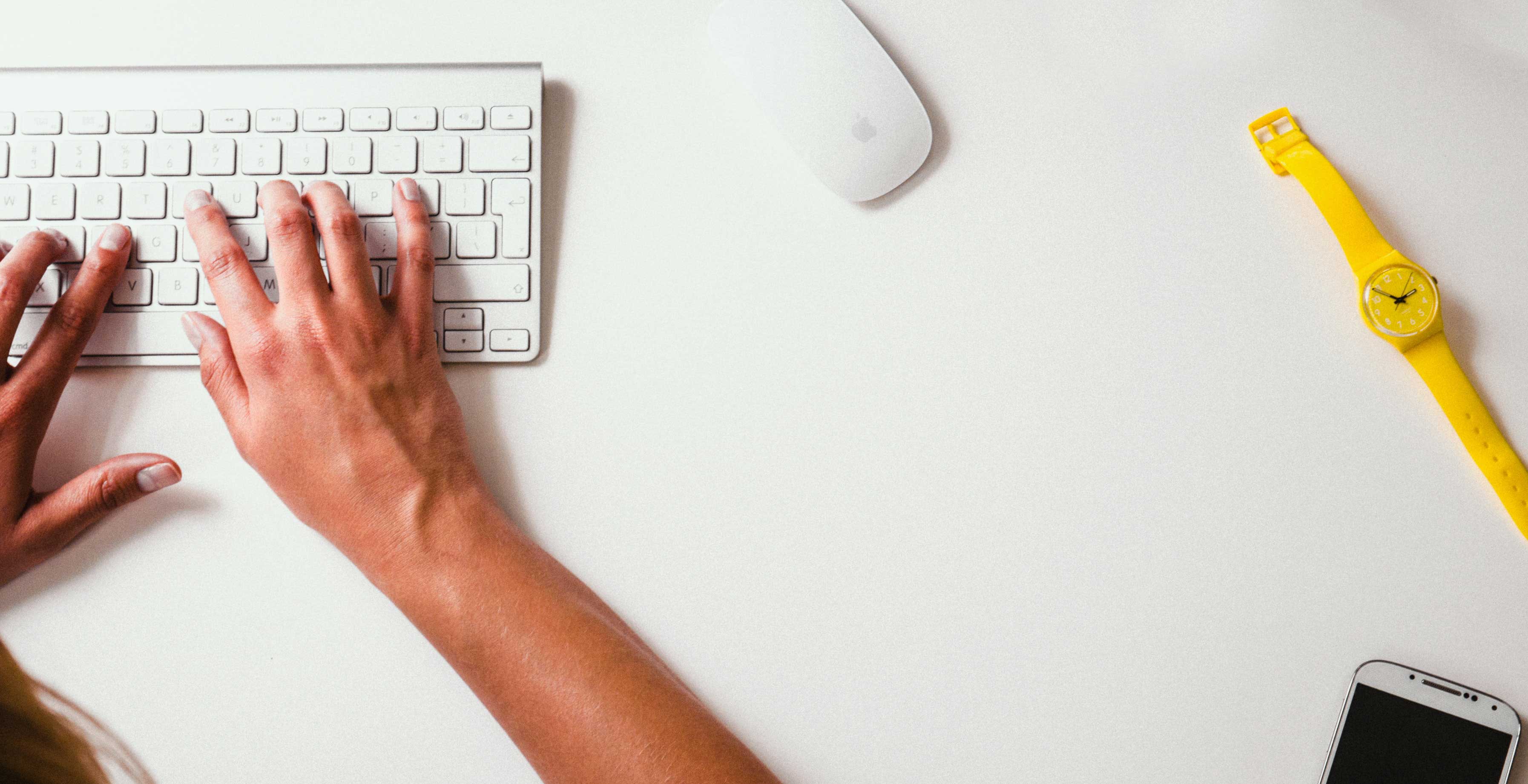 How to Avoid Burnout with a Freelance Side Hustle || a white desk with a yellow watch and someone typing on a keyboard