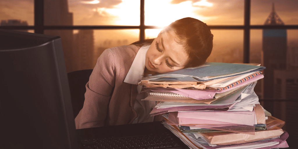 Woman asleep at desk with sun rising in background.