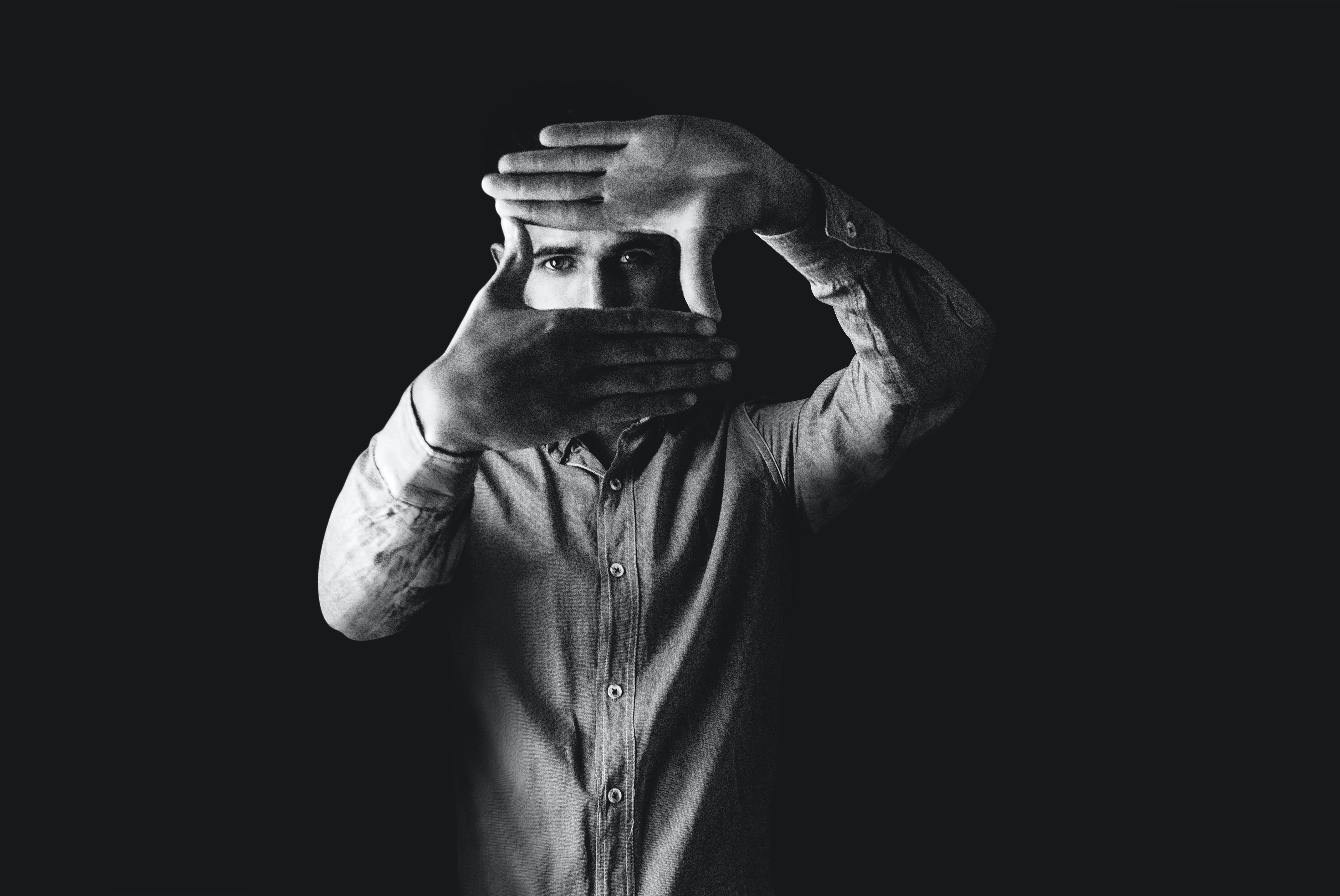 Black and white photo of man looking into the camera through a square he made with his hands