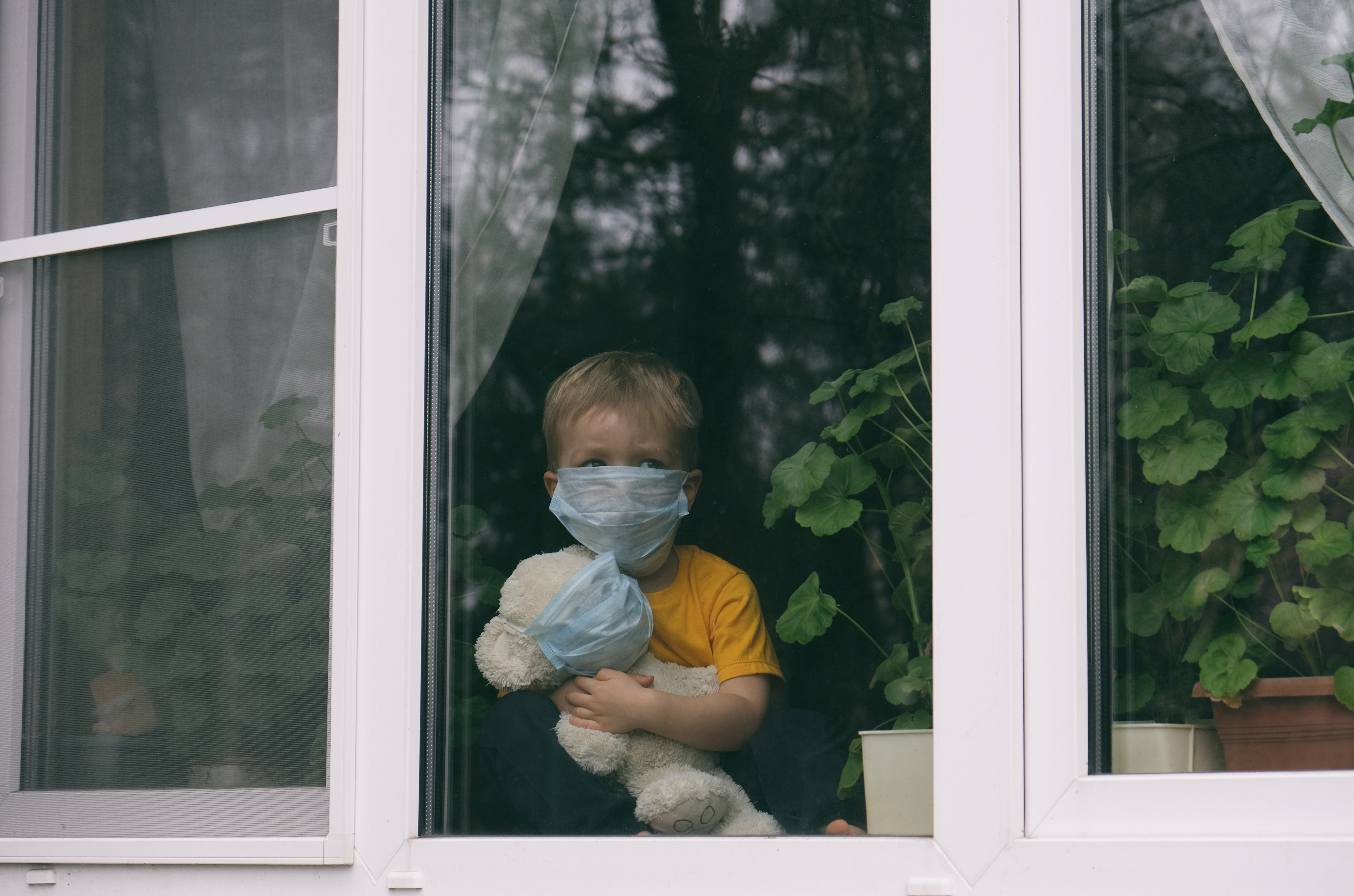 Young child wearing mask looking out window
