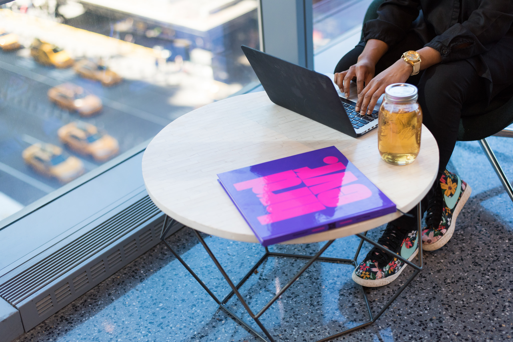 A black woman sits at a table with ice tea and her computer