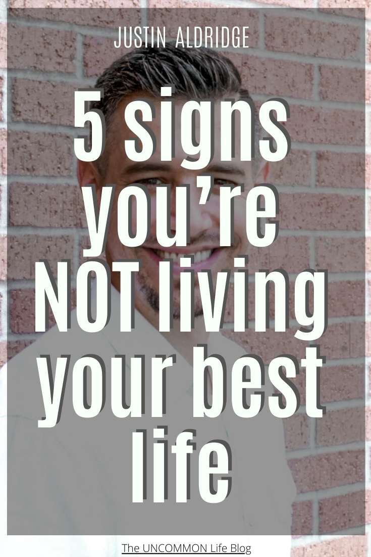 Man in white shirt smiling behind the text, “5 signs you’re NOT living your best life” in white font.