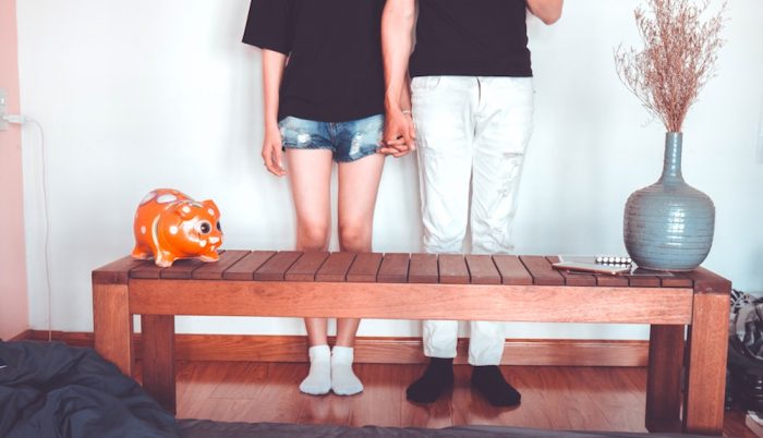 A young couple holding hands and standing in front of a bench at home