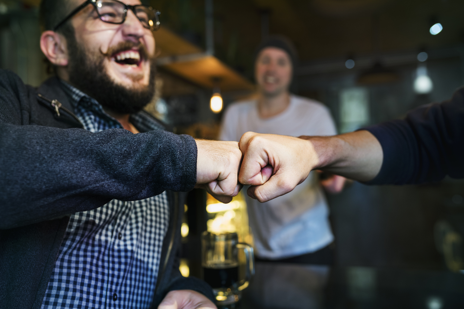 Men fist bumping in a bar, enjoying a drink.