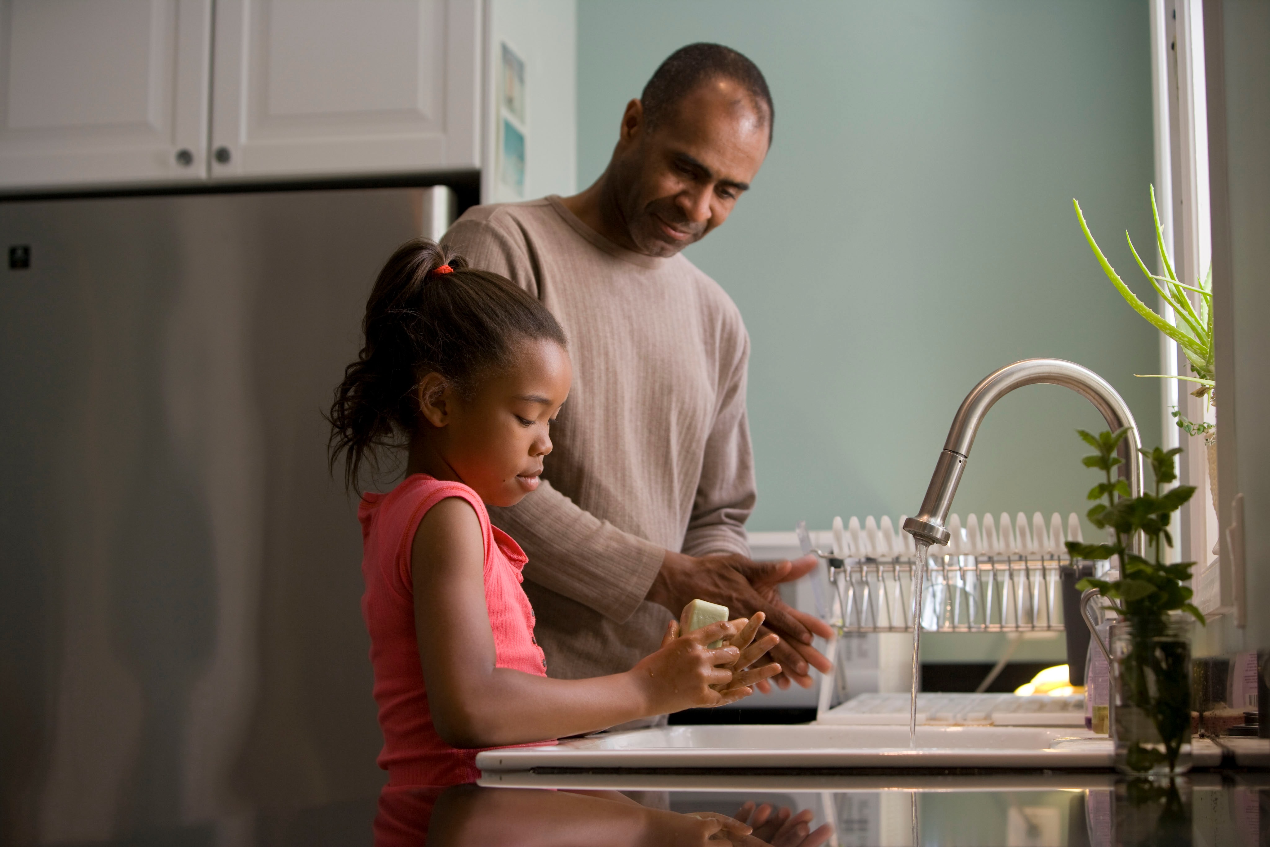 dark skinned man and young girl standing at kitchen counter top talking