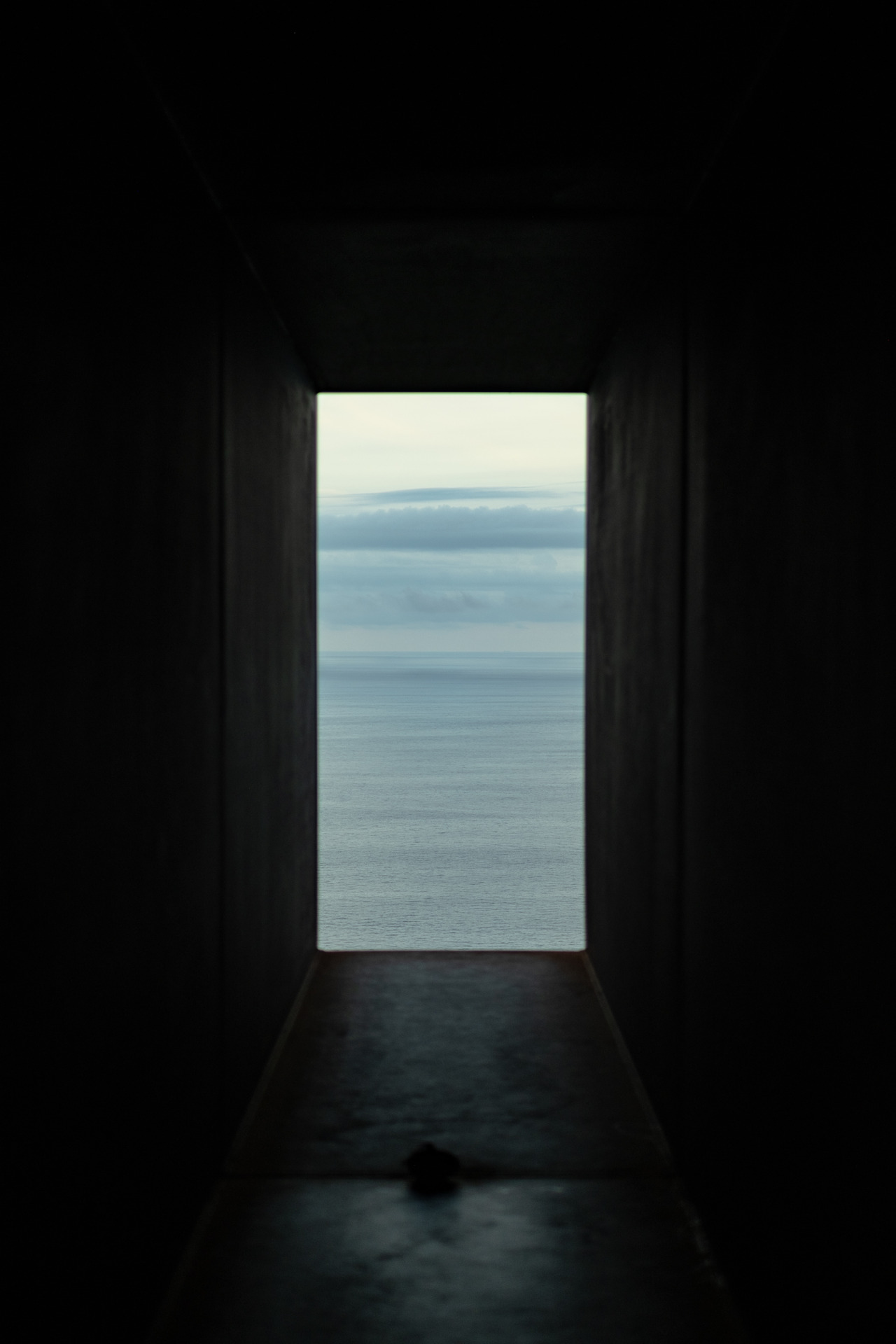 A view of the blue ocean is framed by a dark tunnel