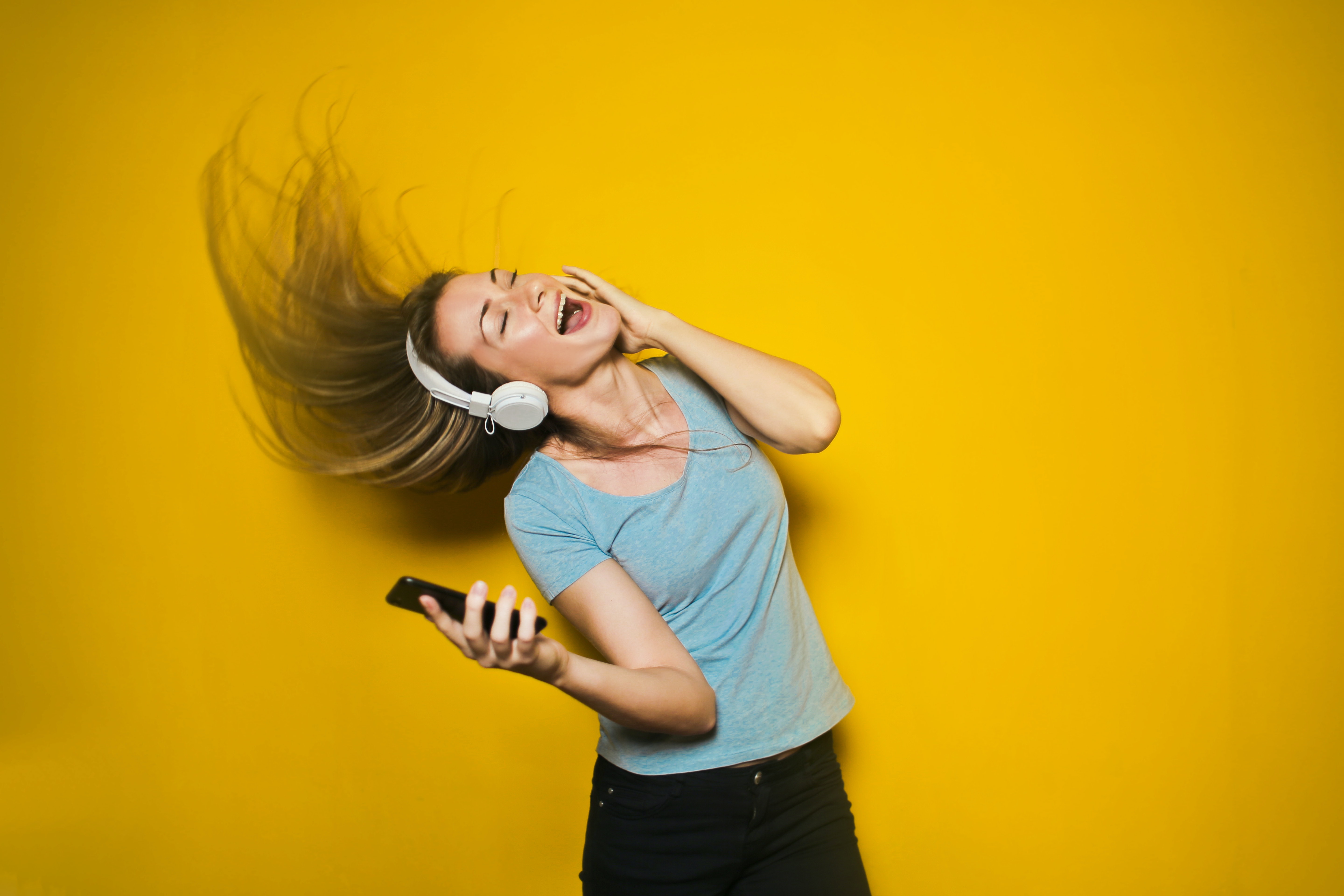 Woman in front of a yellow background whipping her hair while listening to music