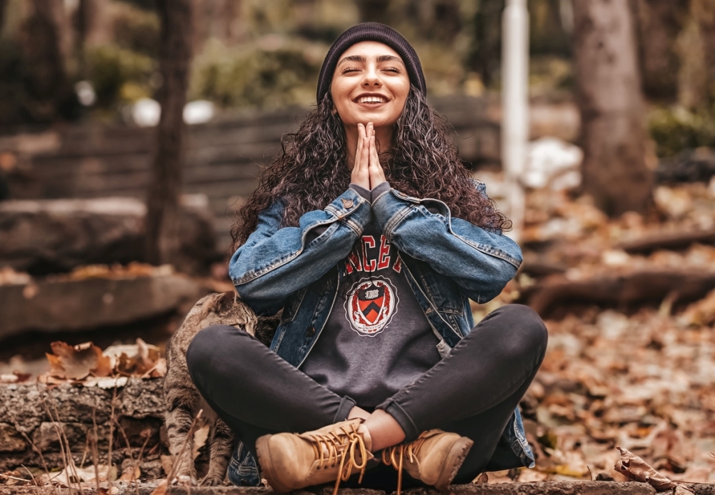 A young female sitting on the ground in a meditating position while smiling