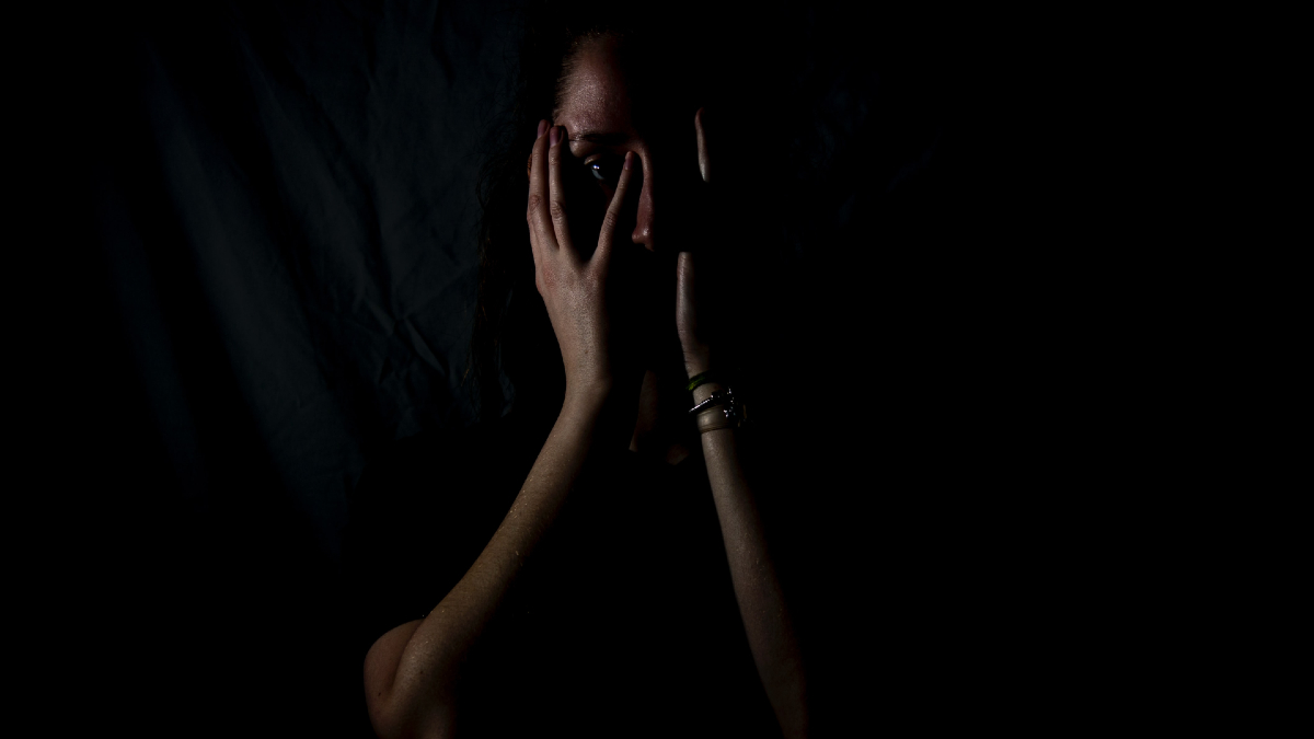A woman lies in the dark with her face in her hands.