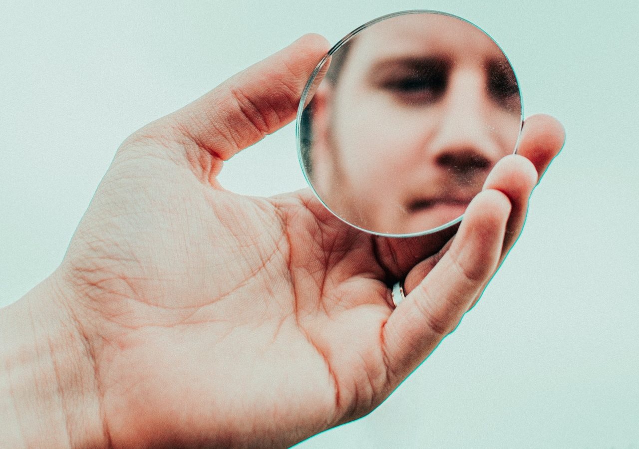A man looking on the reflection of himself on a small round mirror