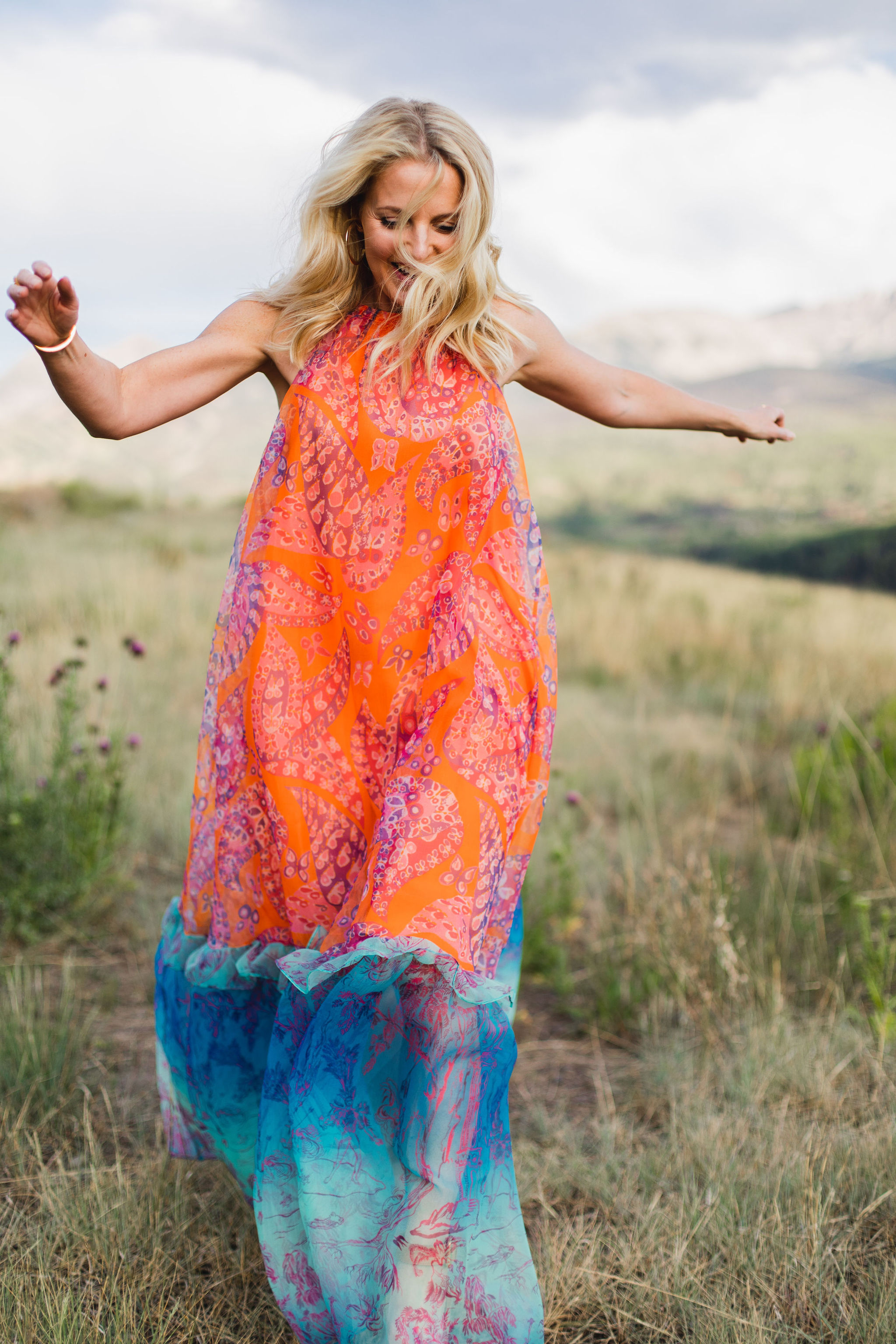 blonde woman wearing trapeze dress in bright colors running through grassy field