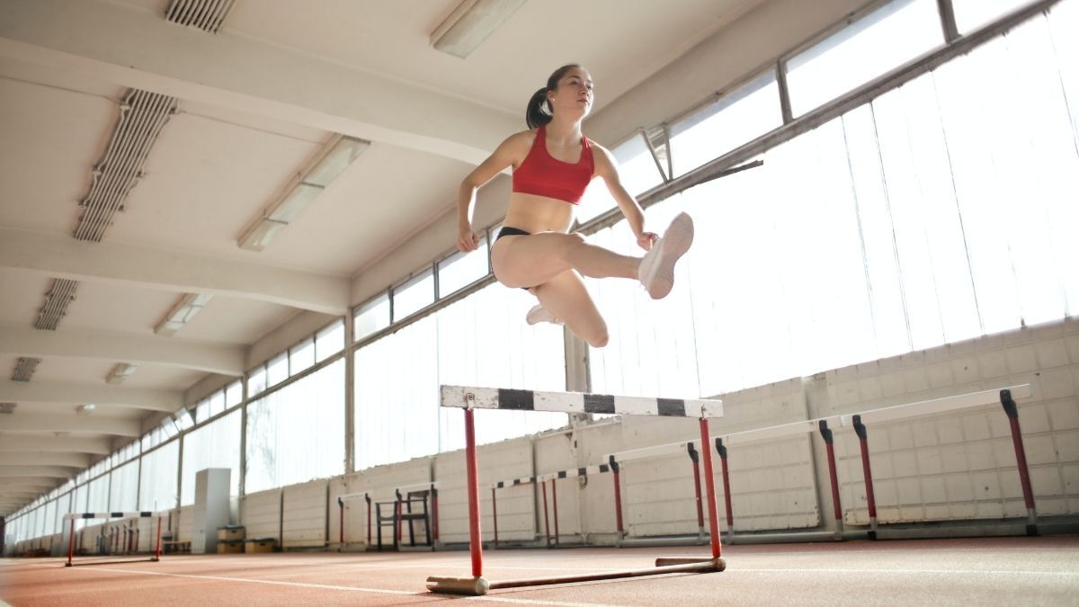 A young woman running and jumper over a hurdle