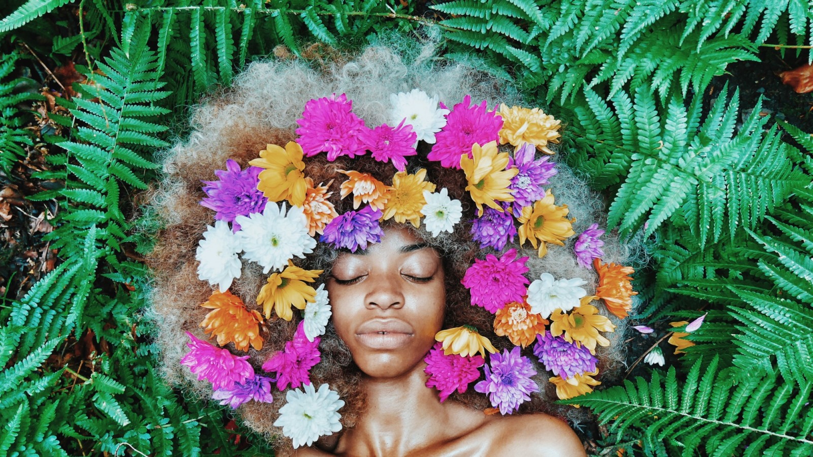 Black woman with flowers in her hair surrounded by plants.