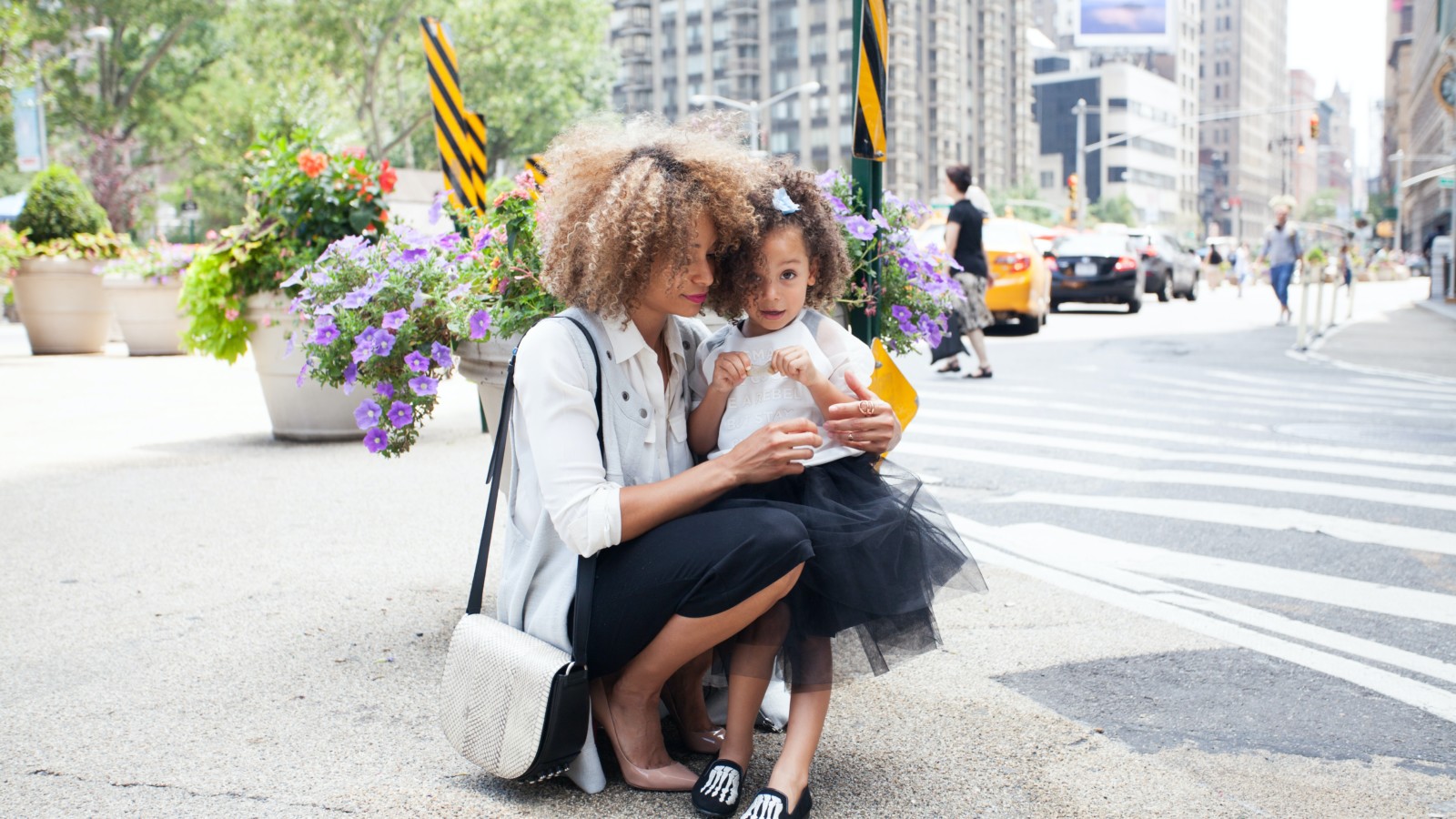 Working Black mom kneeling with daughter on city street