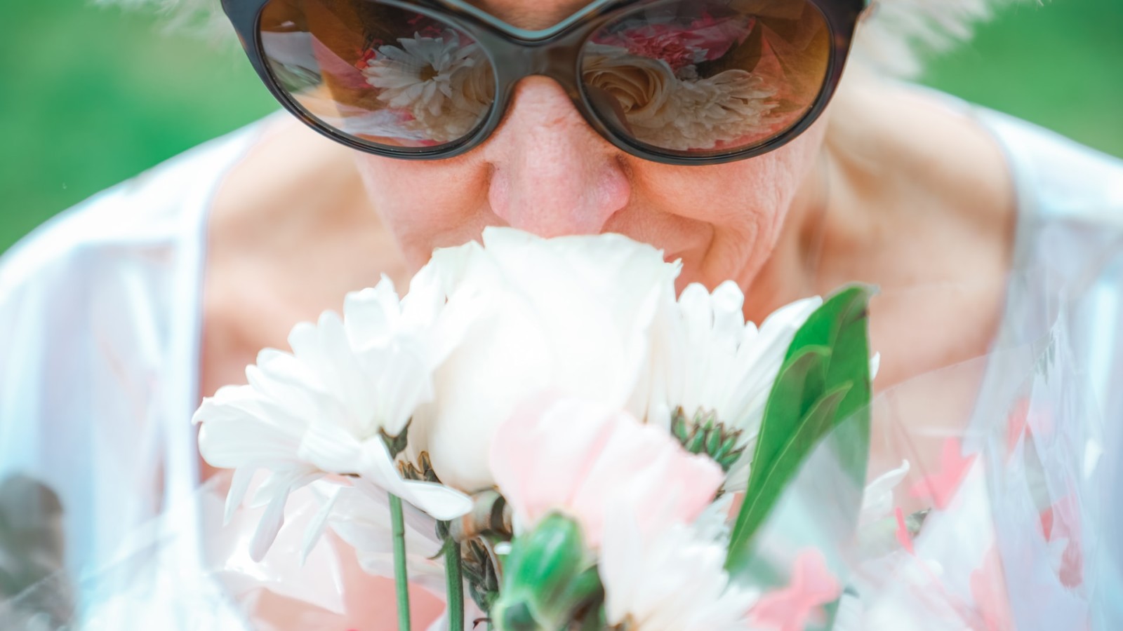 old woman wearing sunglasses smelling flowers