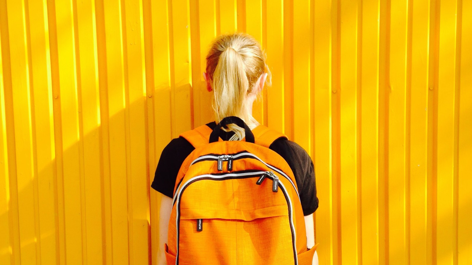Woman with backpack on facing a yellow wall