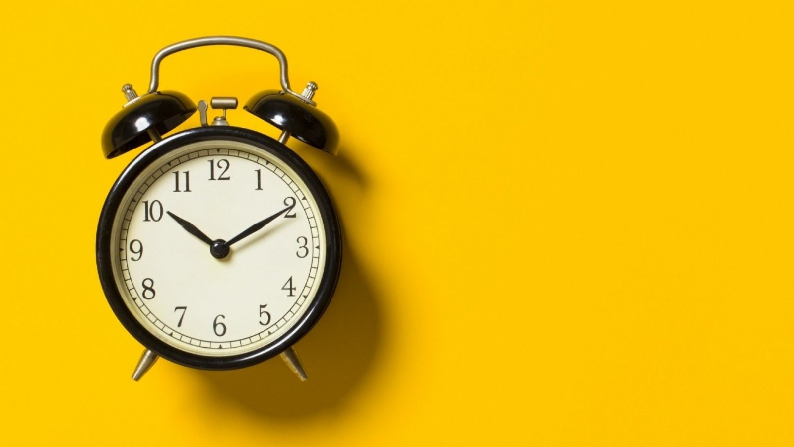 An image of an old-fashioned alarm clock on a yellow background