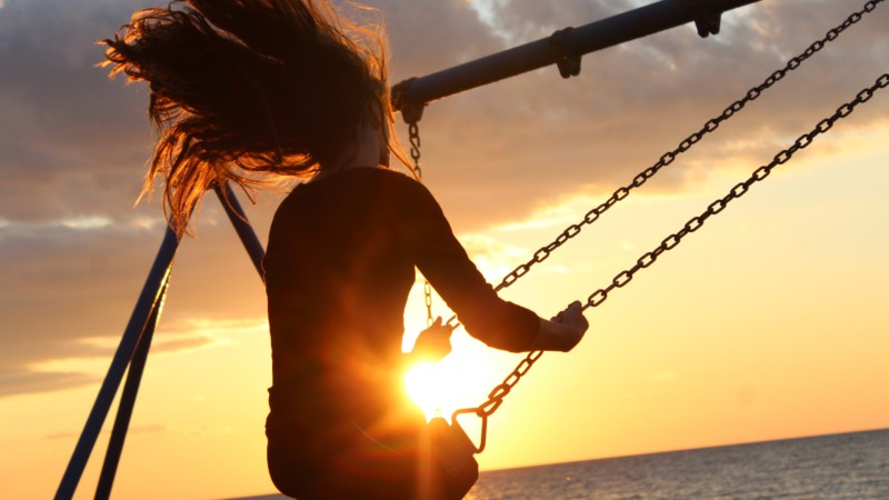 girl on swing at sunset by beach