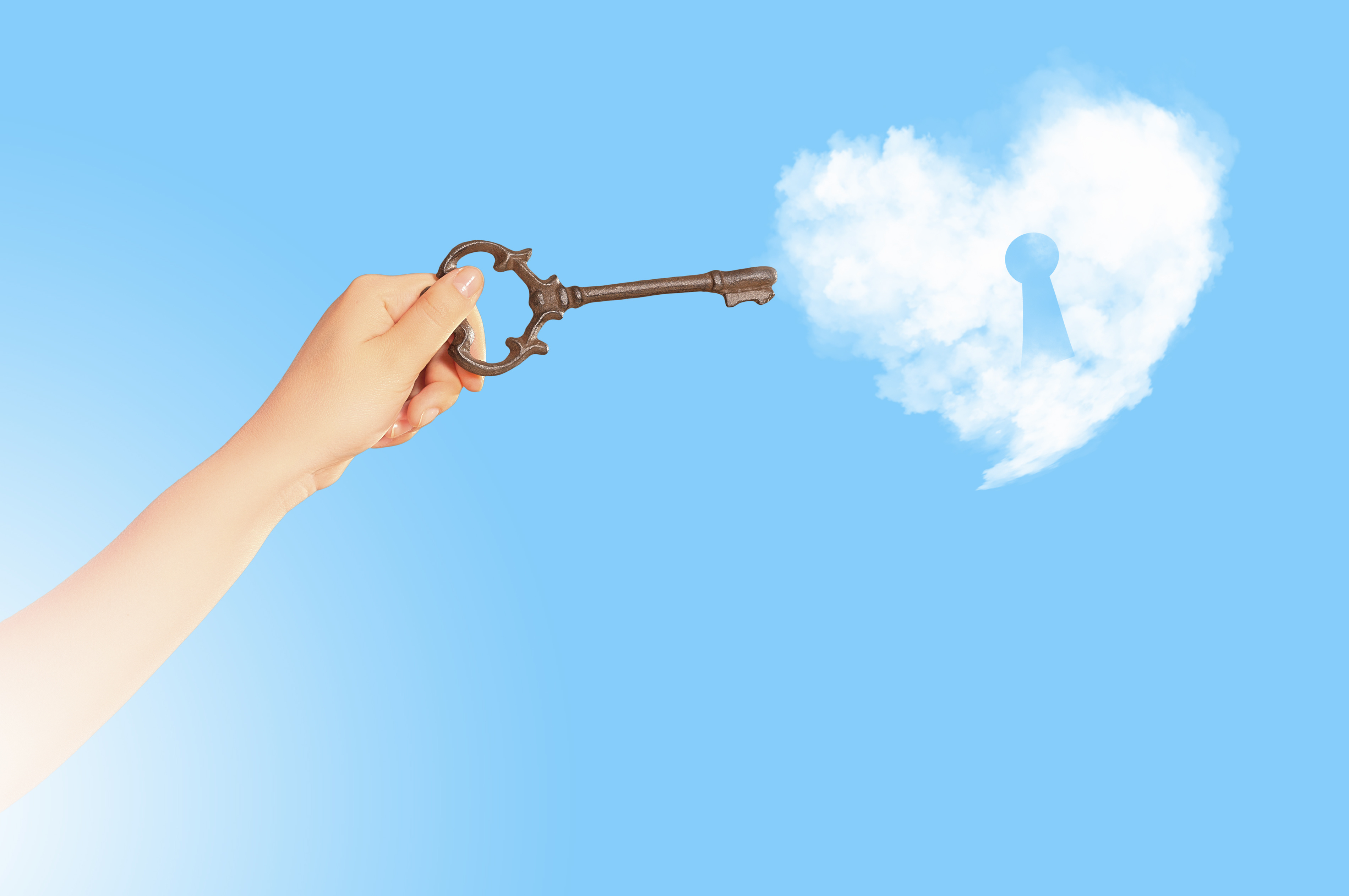 An old fashioned key is held up to a heart shaped cloud with a key hole in it that fits the key in the woman's hand holding it.  The background is sky blue.