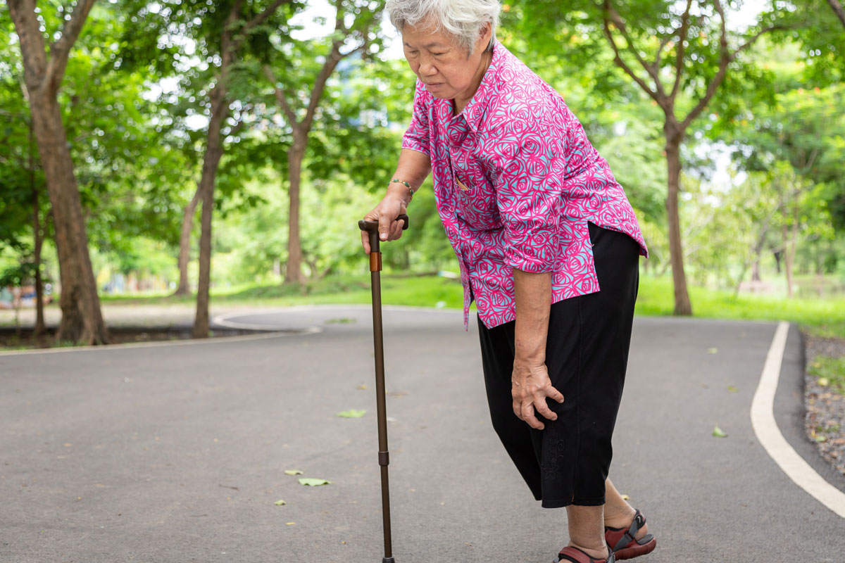 Elderly Asian woman walking with cain, but in pain.