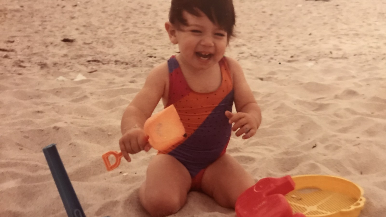 Xian on the beach with a shovel giggling age 1