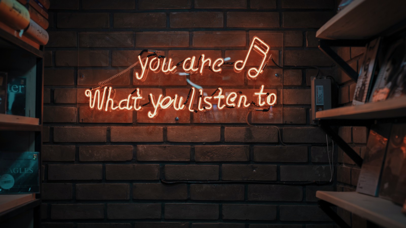 Photo of you are what you listen to text spelled in lights by music notes on brick wall. Photo on Dr. James Goydos 2021 article on physician health podcasts