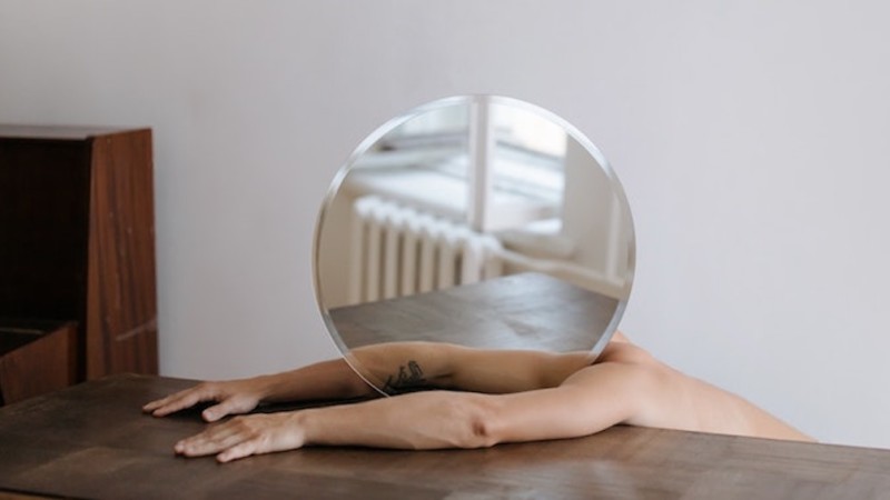 A man splayed out on a table with a round mirror next to his head