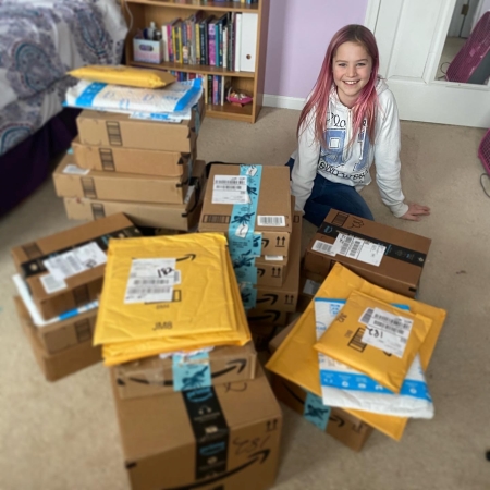 Girl poses with pile of boxes and shipping envelopes.