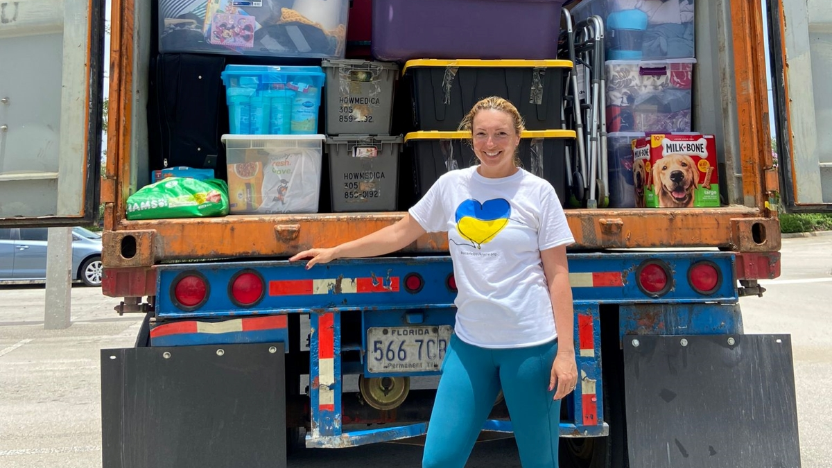 Woman poses in front of a truck filled with humanitarian supplies.