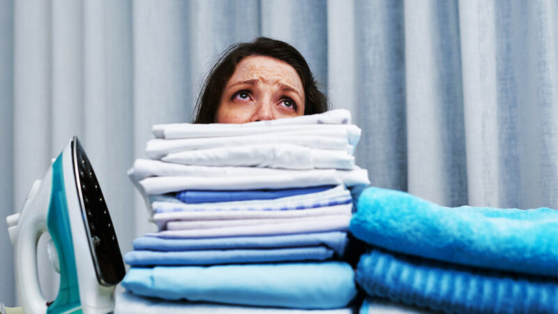 Overwhelmed woman behind tall stack of folded laundry.