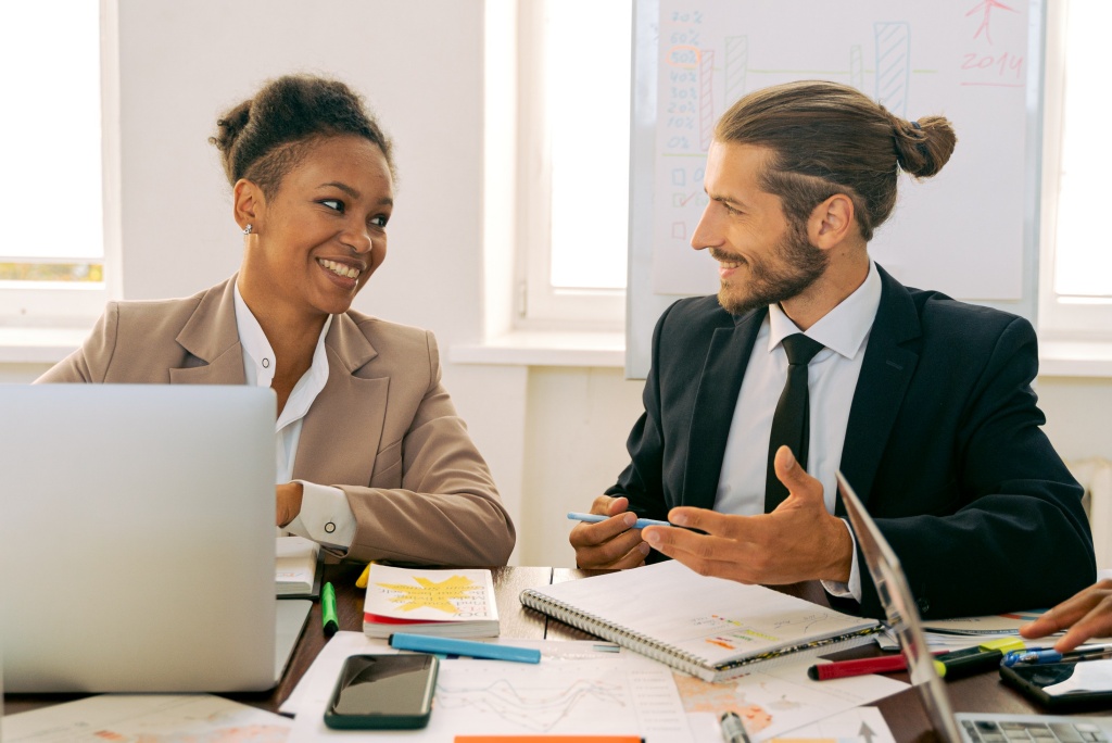 black woman and white man smiling while in a work meeting