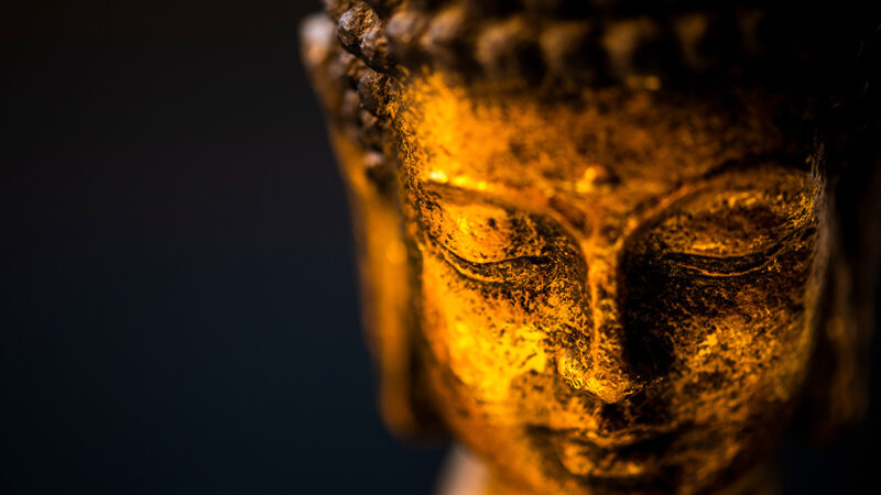 Close up of ancient Buddha sculpture bathed in glden light.