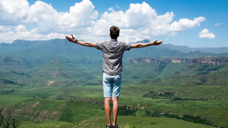 Photo of a person standing at the top of a plateau while proudly viewing beautiful landscape below