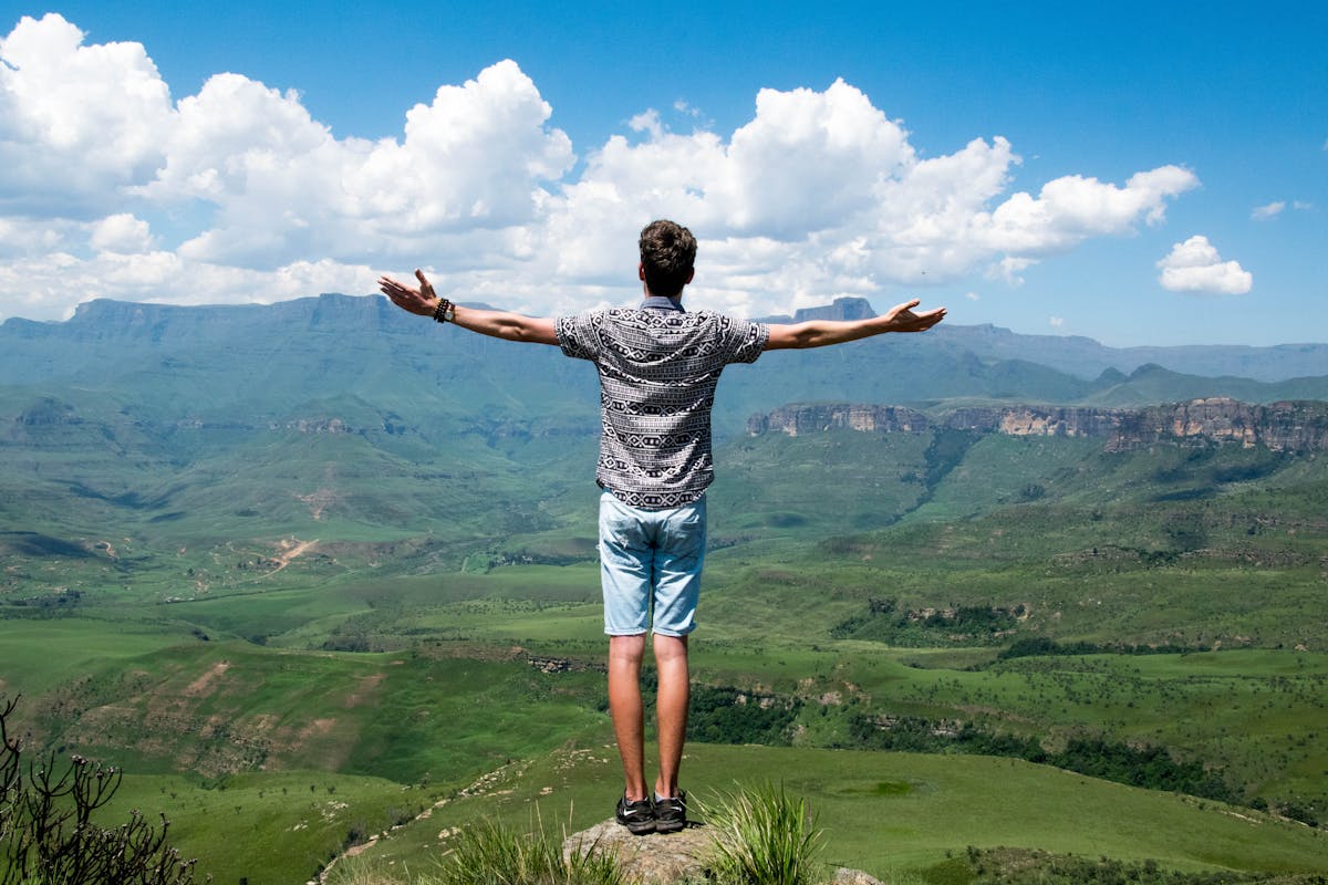 Photo of a person standing at the top of a plateau while proudly viewing beautiful landscape below